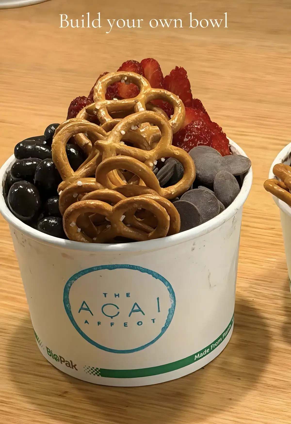 Build-your-own acai bowl in a takeaway cup, topped with pretzels, strawberries and chocolate pieces