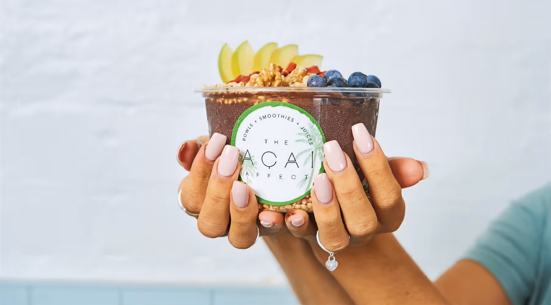 Two hands holding an acai bowl topped with apple, blueberries, goji and walnuts